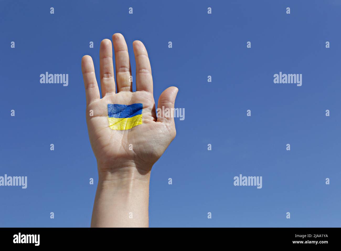 Gros plan d'une main de femme éclairée par le soleil avec drapeau national ukrainien dessiné sur fond bleu ciel. Une main levée dans un support d'Ukra Banque D'Images