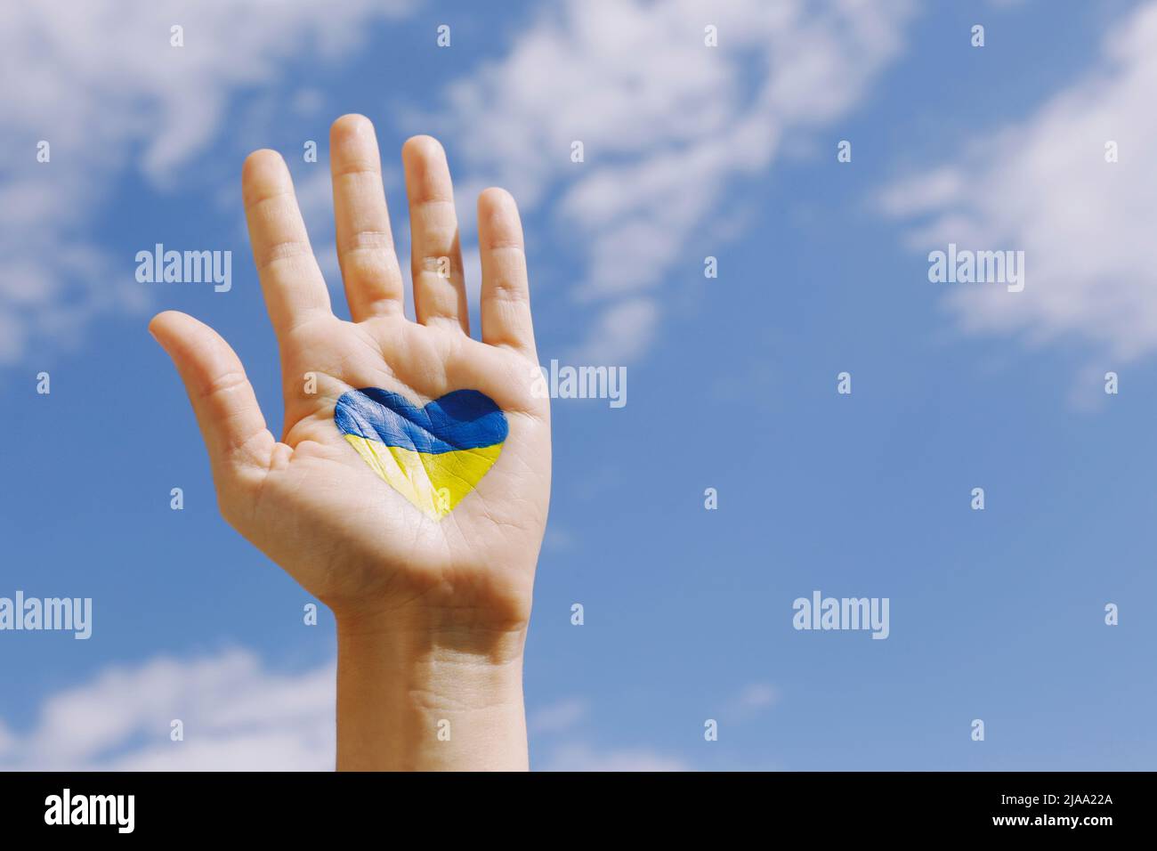 Gros plan de la main d'une femme au soleil avec le drapeau national ukrainien en forme de coeur dessiné dessus sur fond bleu ciel. Une main levée dans un Banque D'Images