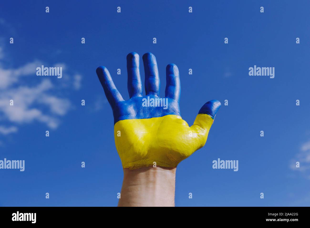 Gros plan sur la main d'un homme illuminée par le soleil peint en couleurs du drapeau national ukrainien. .Une main levée sur fond bleu ciel comme symbole de sup Banque D'Images