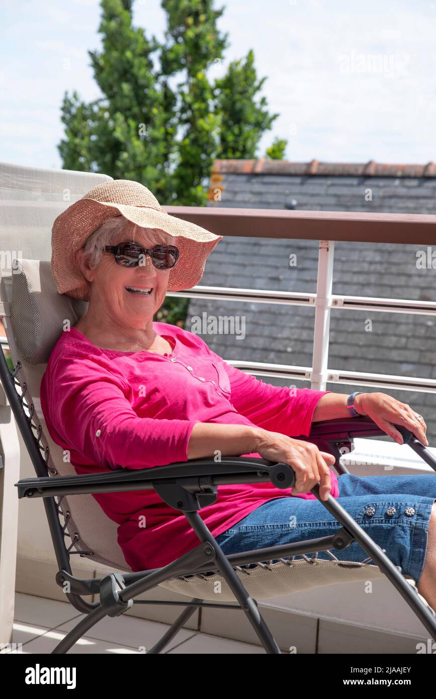 Une femme âgée souriante assise dans une chaise longue sur la terrasse d'un appartement Banque D'Images