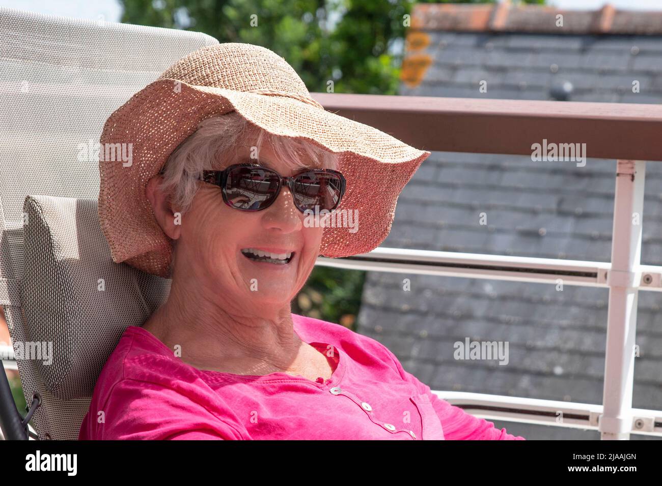 Une femme âgée souriante assise dans une chaise longue sur la terrasse d'un appartement Banque D'Images