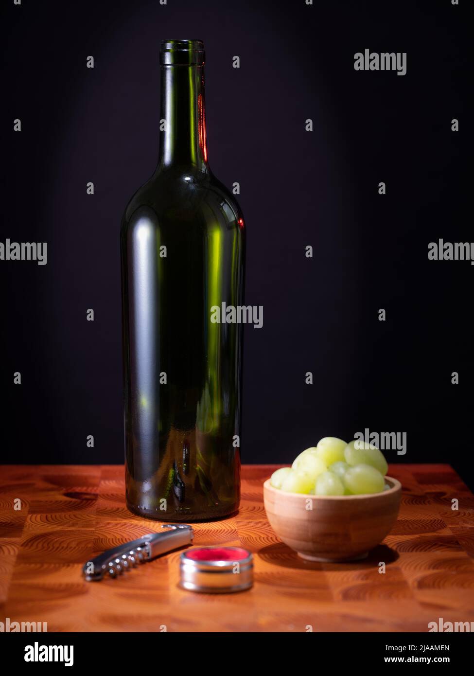 Helsinki / Finlande - 29 MAI 2022 : une bouteille de vin rouge vide, un verre de vin et quelques raisins sur une surface en bois sur fond sombre. Banque D'Images