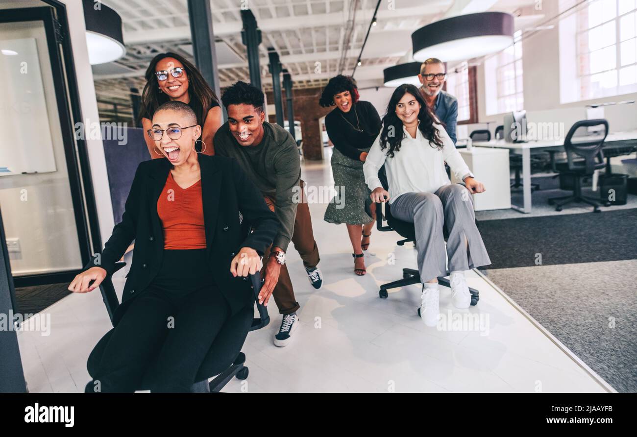 Amusez-vous au bureau. Groupe heureux de collègues se poussant les uns les autres sur des chaises dans un bureau créatif. Une équipe d'hommes d'affaires qui s'amusent et célèbrent Banque D'Images