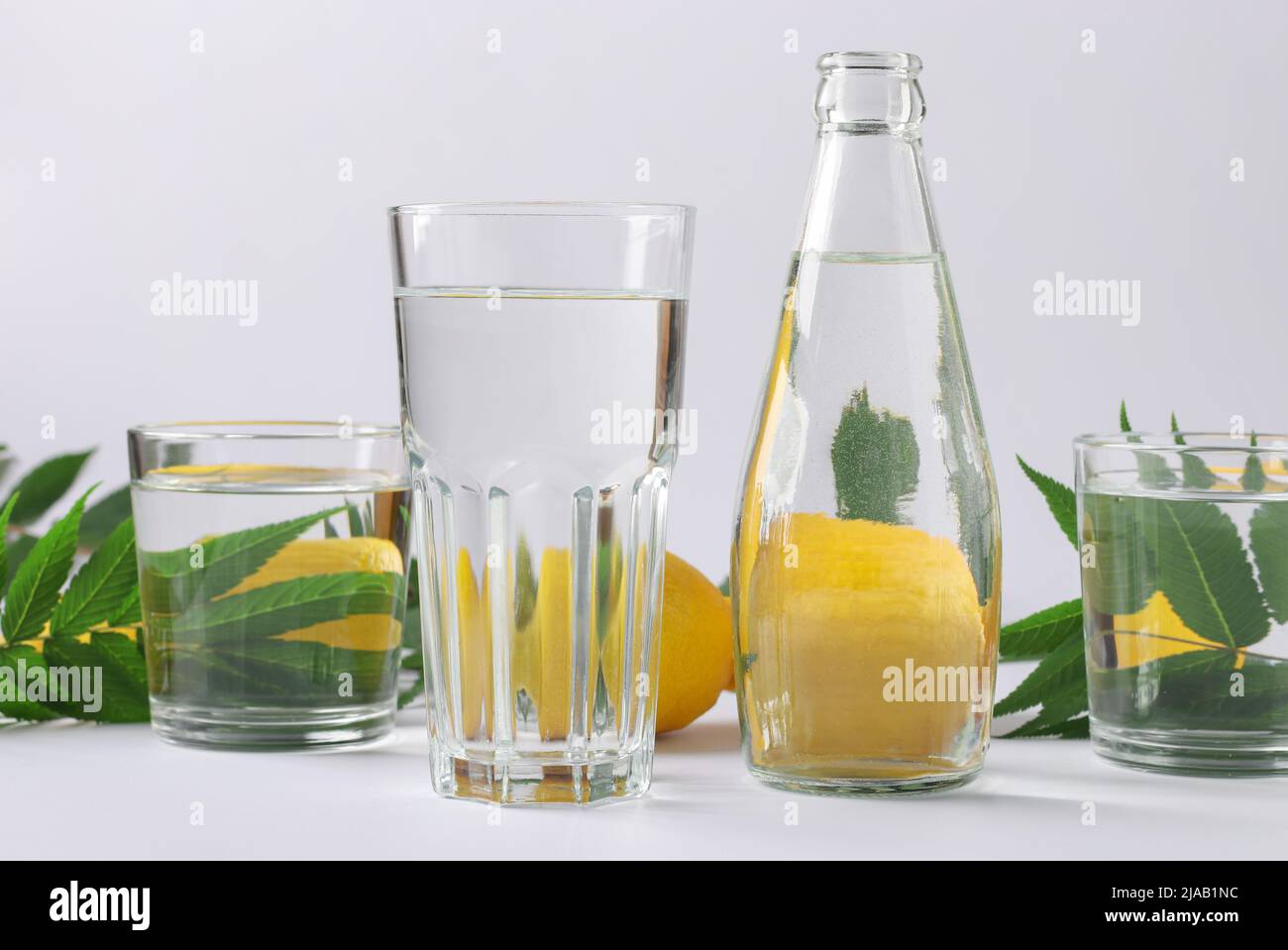Déformation d'un objet par des récipients transparents remplis d'eau. Illusions optiques. Les citrons déformés et les feuilles vertes se trouvent derrière des récipients en verre Banque D'Images