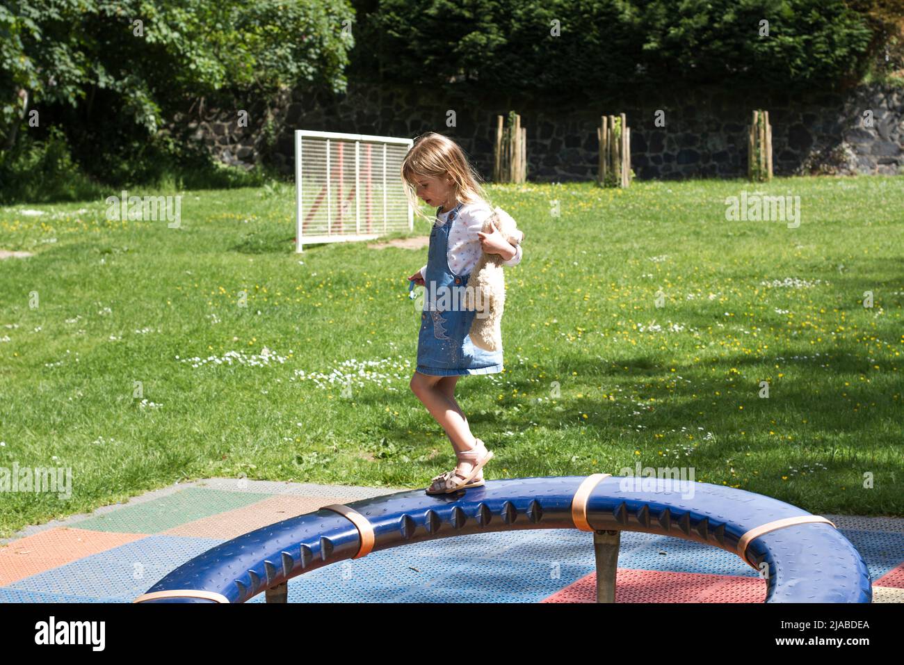 Une fille de 5 ans joue dans le parc tout en tenant son ours en peluche Banque D'Images