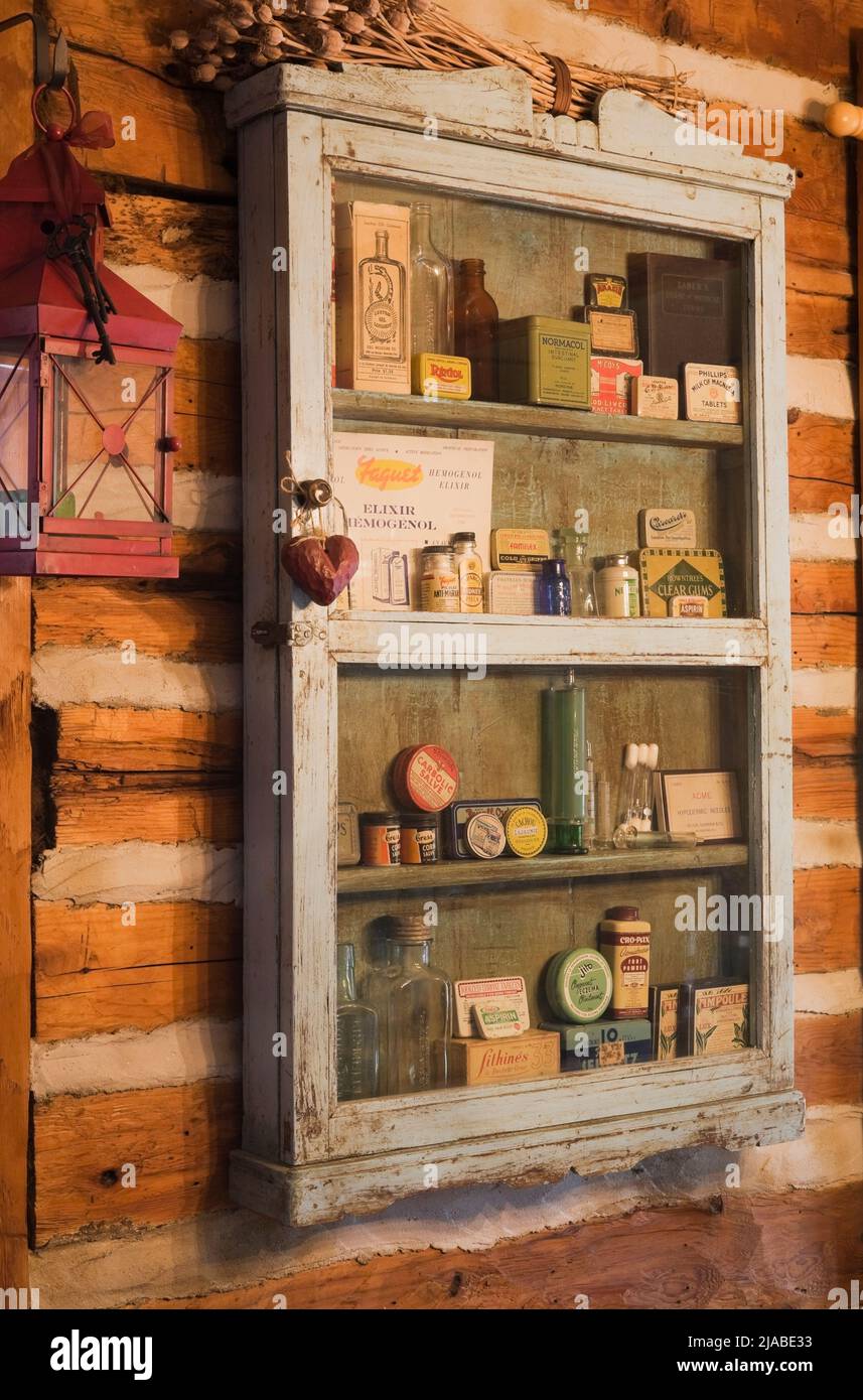 Gros plan d'une armoire de médecine ancienne avec de vieilles bouteilles de pilules, des boîtes de pommade sur le mur de la salle à manger à l'intérieur de l'ancienne cabane en rondins de style cottage Canadiana vers 1825. Banque D'Images