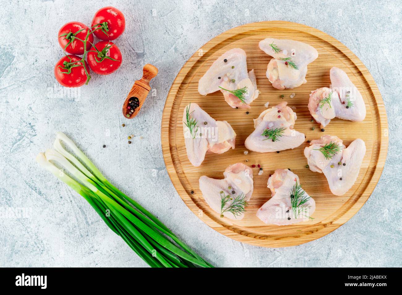 Les ailes de poulet crues reposent sur un support rond sur un fond clair avec des épices. Banque D'Images