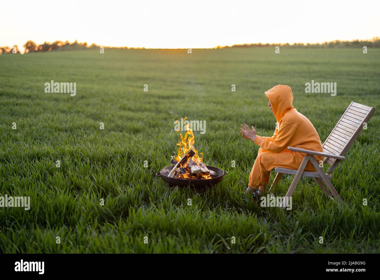 Jeune personne assise près de la cheminée sur un terrain vert au coucher du soleil Banque D'Images