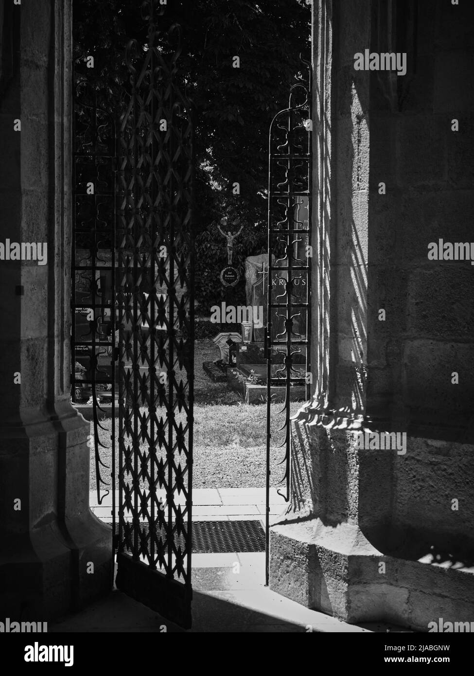 Vue de l'église par la porte en treillis métallique entrouverte du cimetière en noir et blanc Banque D'Images