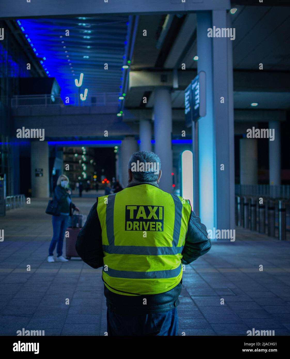 Portrait arrière d'un chauffeur de taxi debout dans le terminal 2 de l'aéroport de Manchester, en attente des clients. Banque D'Images
