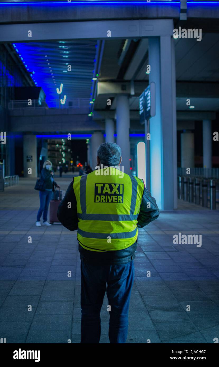 Portrait arrière d'un chauffeur de taxi debout dans le terminal 2 de l'aéroport de Manchester, en attente des clients. Banque D'Images