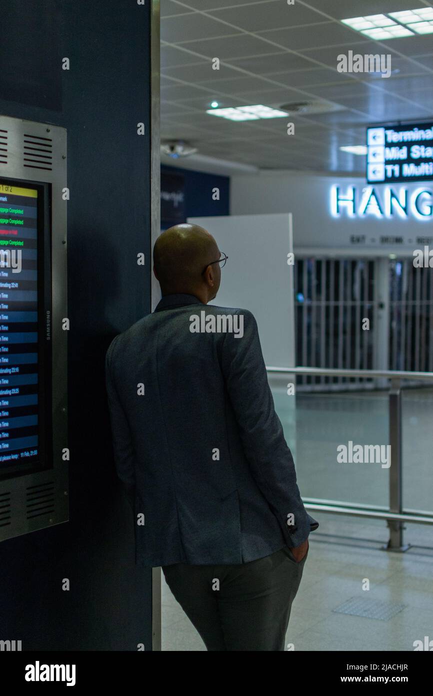 Homme décontracté appuyé contre le mur, attendant les arrivées à l'aéroport international de Manchester, Grand Manchester, Royaume-Uni. Banque D'Images