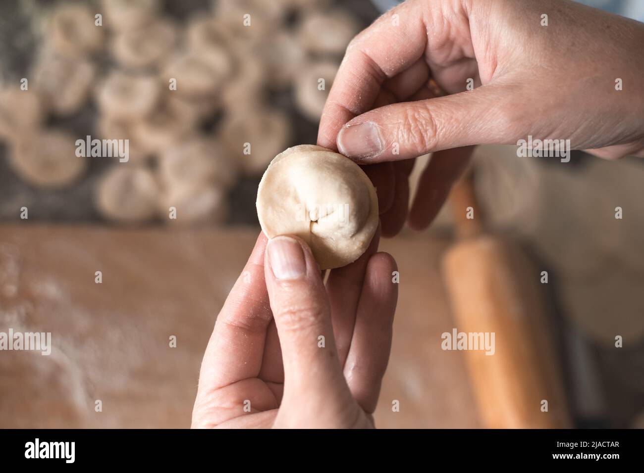 Une femme sculpte des boulettes de pâte avec garniture de viande dans la cuisine. Cuisson de délicieux boulettes maison. Banque D'Images