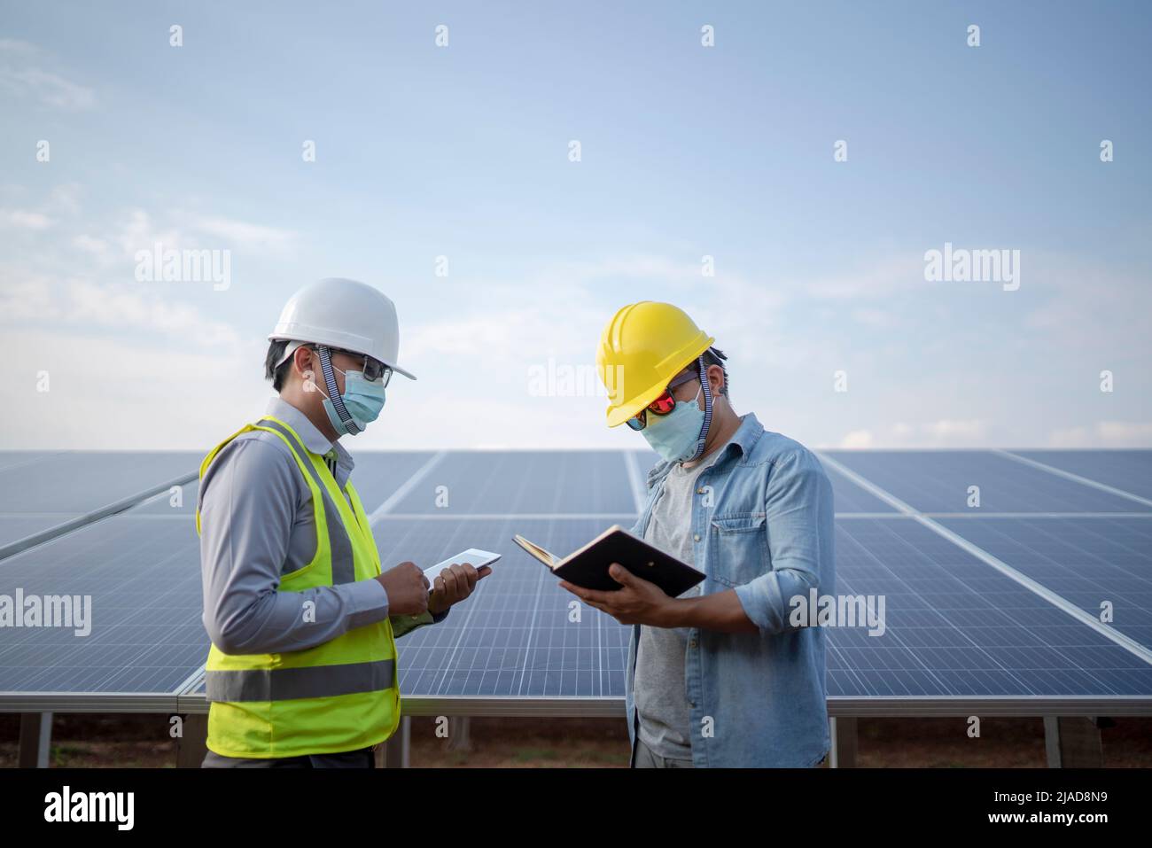 Deux ingénieurs se tenant à côté de panneaux solaires dans une station solaire regardant un ordinateur portable et une tablette numérique, Thaïlande Banque D'Images