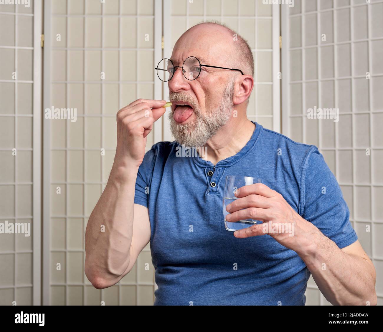 l'homme âgé prend un médicament ou un supplément de pilule avec un verre d'eau à la maison, concept de santé d'auto-soins Banque D'Images