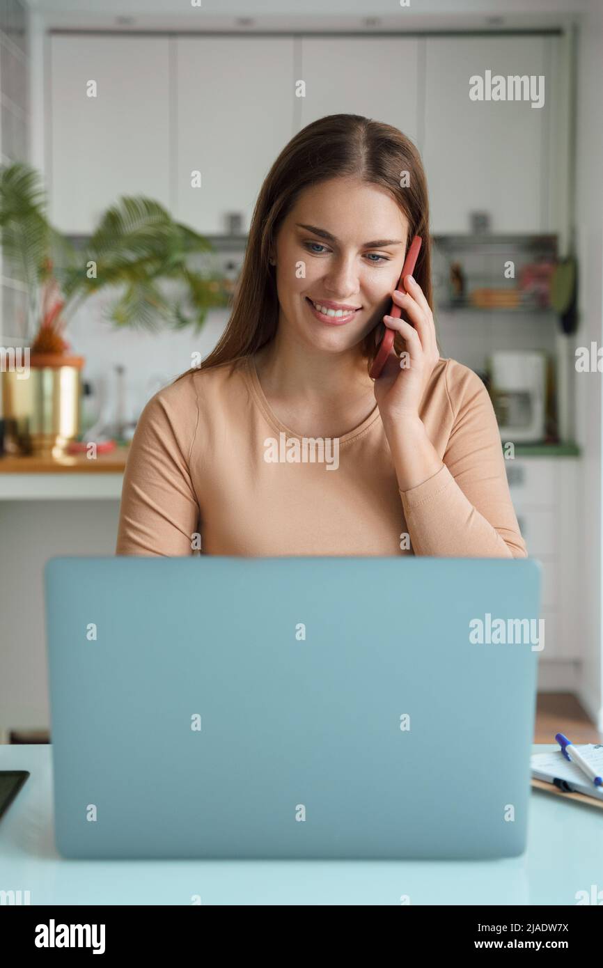Portrait d'une jeune femme répondant à un appel mobile pendant un travail en ligne sur un ordinateur portable Banque D'Images