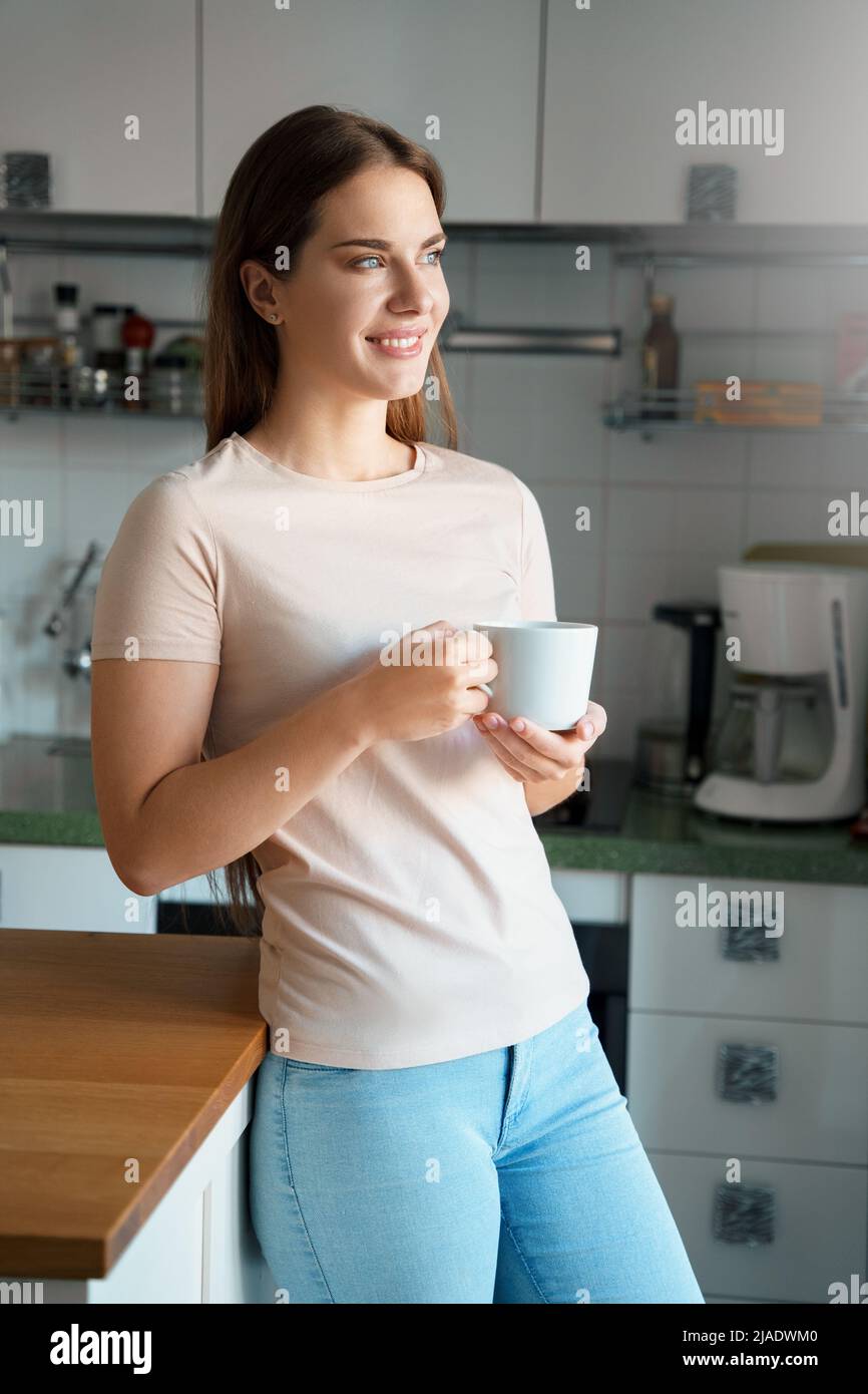 Jeune femme heureuse de boire du café dans la cuisine du bureau à la maison le matin Banque D'Images