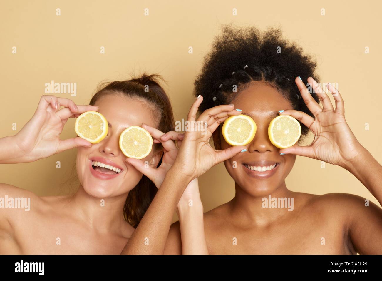 Cercles d'agrumes colorés près du visage de femmes multiraciales gaies souriant et tenant des agrumes frais près des yeux tout en représentant la vitamine C ben Banque D'Images