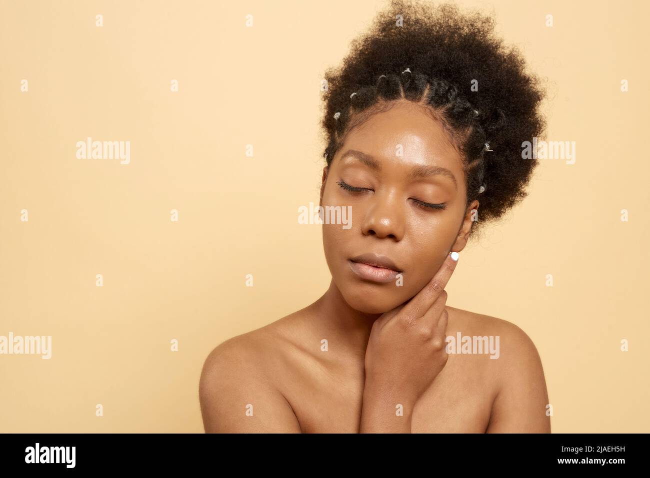 Une belle jeune femme afro-américaine touche la peau délicate de son visage. Bonne beauté africaine femme après soin spa isolé sur beige avec c Banque D'Images