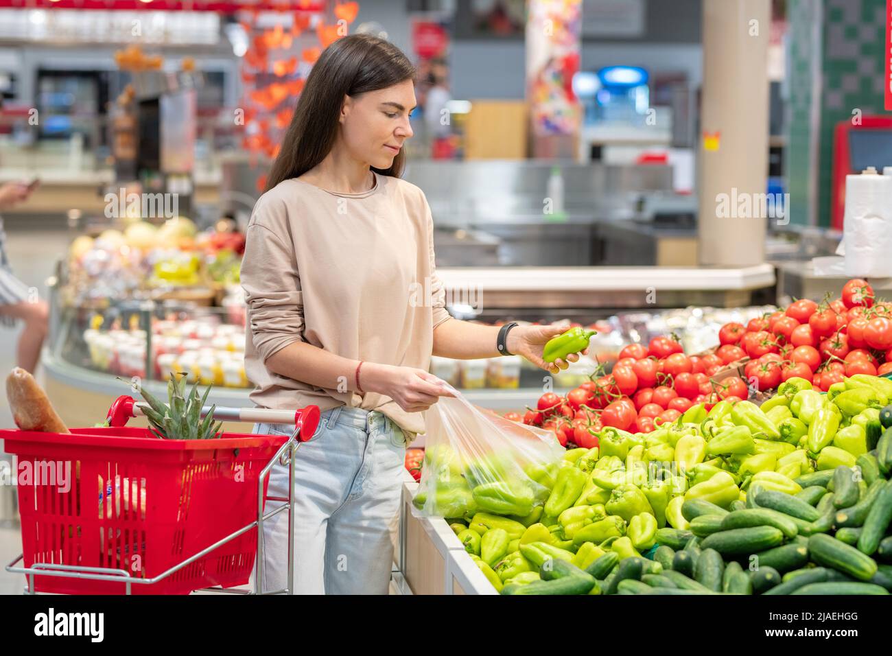 Portrait d'une jeune femme adulte au supermarché avec des magasins panier de sélection de poivrons doux Banque D'Images