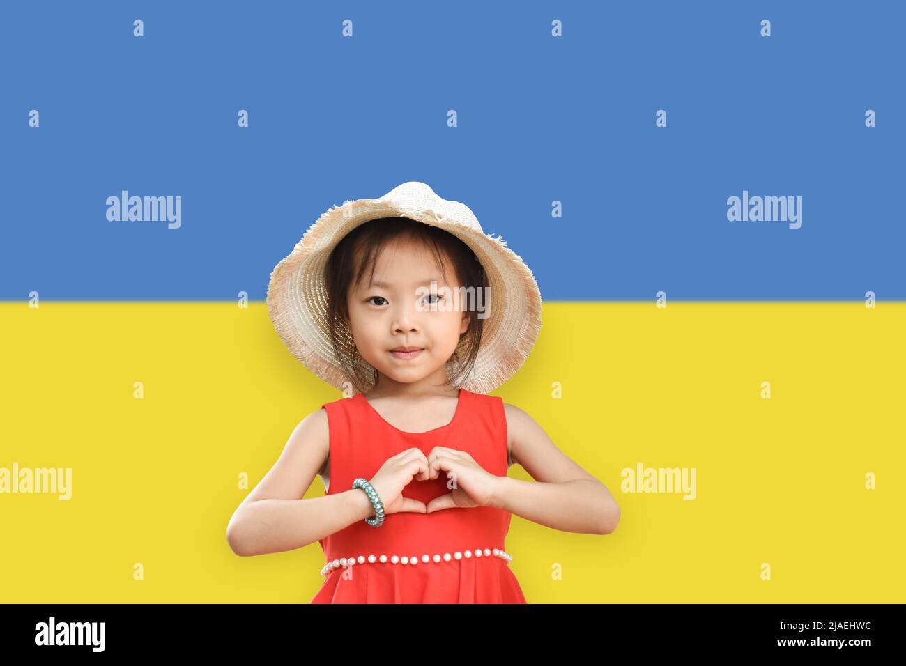 Petite fille porter chapeau montrant les mains en forme de coeur sur l'Ukraine drapeau couleur fond. Arrêter la guerre pour la paix. Love Ukraine concept. Banque D'Images