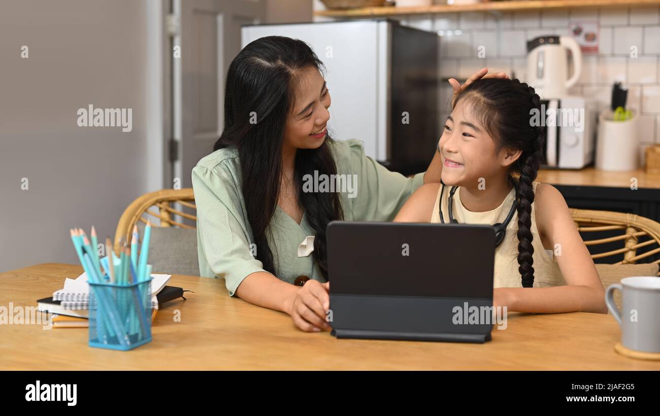 Une maman asiatique attentionnée aide sa fille à faire ses devoirs, étudiant en ligne dans la cuisine Banque D'Images