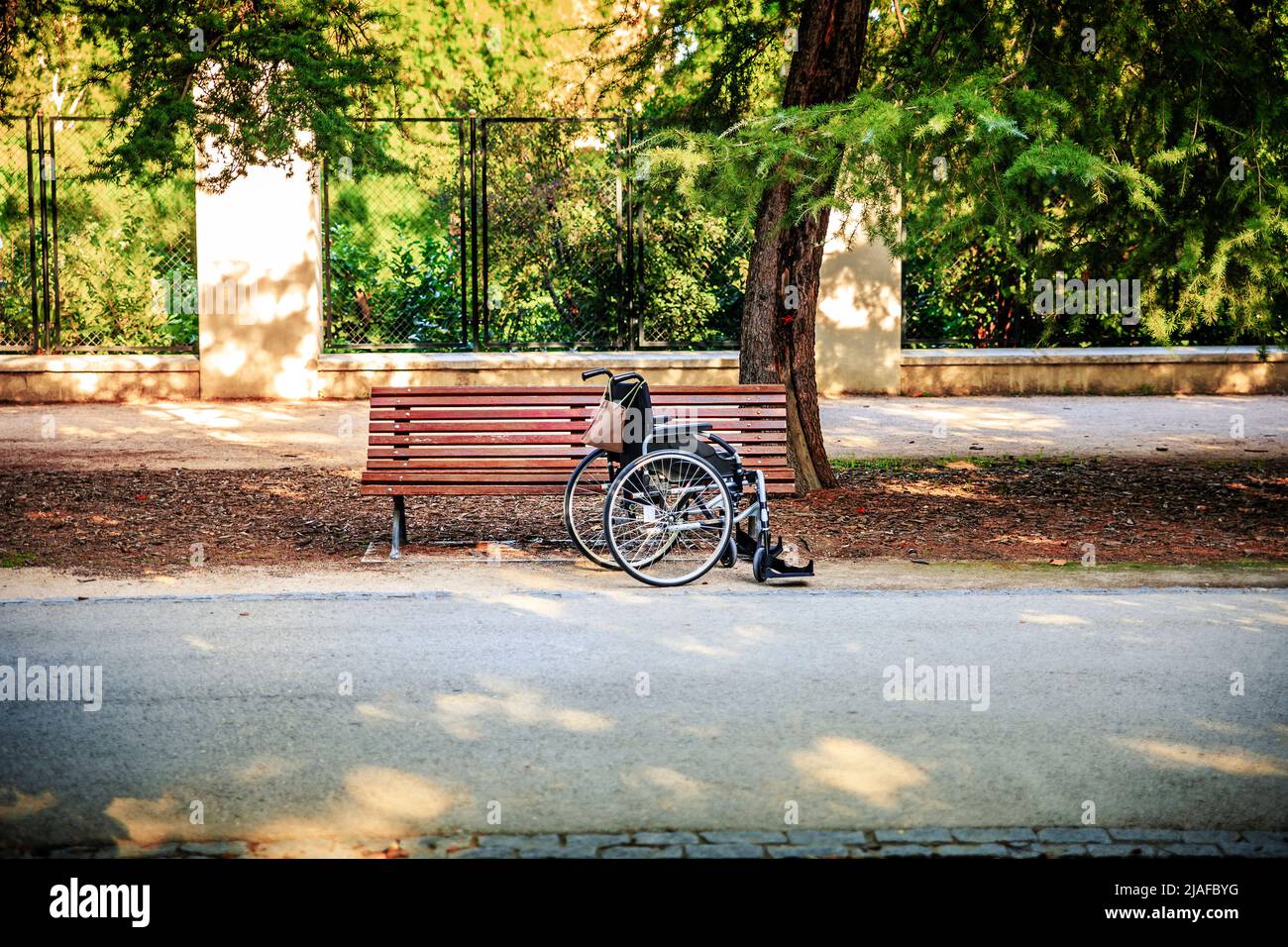 fauteuil roulant vide à l'extérieur d'un parc à côté d'un banc de parc Banque D'Images