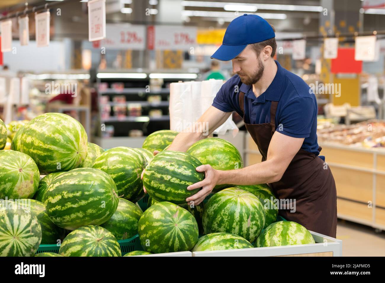 Travailleur de supermarché non reconnaissable portant un uniforme exposant des pastèques fraîches, espace de copie Banque D'Images