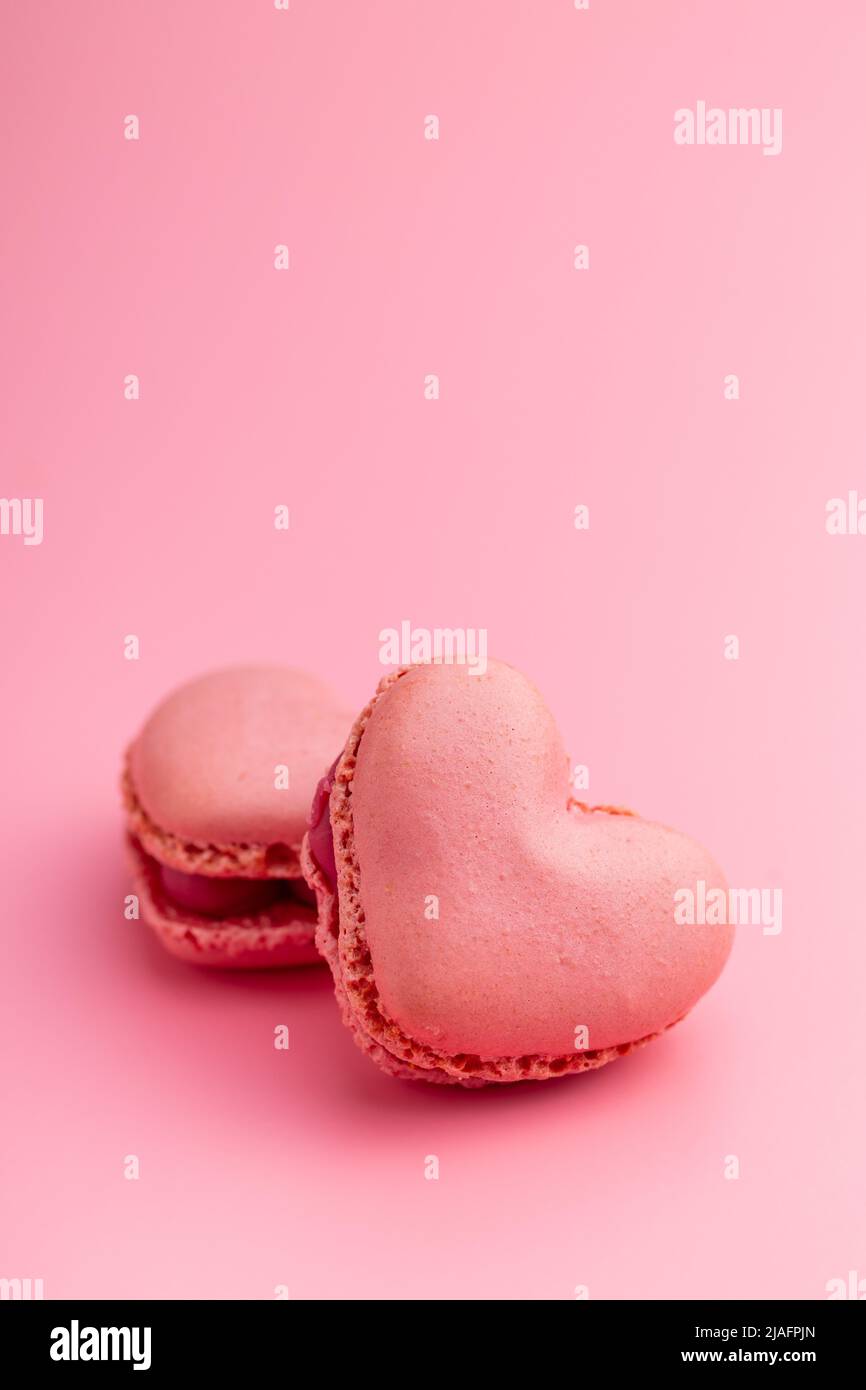 Macarons doux en forme de cœur sur fond rose. Banque D'Images