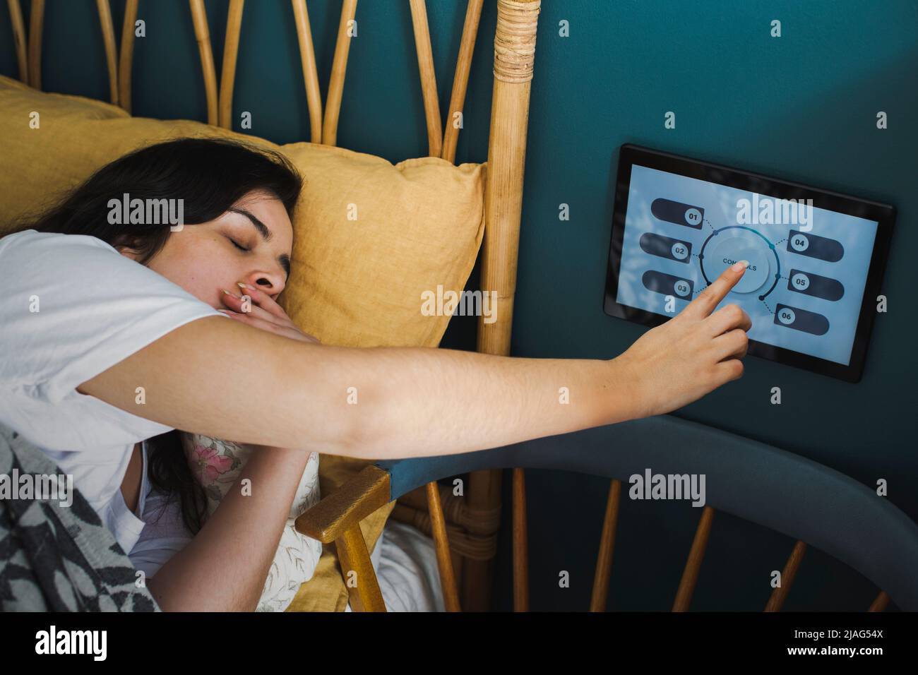 Femme bâillant tout en utilisant un appareil d'automatisation domestique sur le mur dans la chambre Banque D'Images