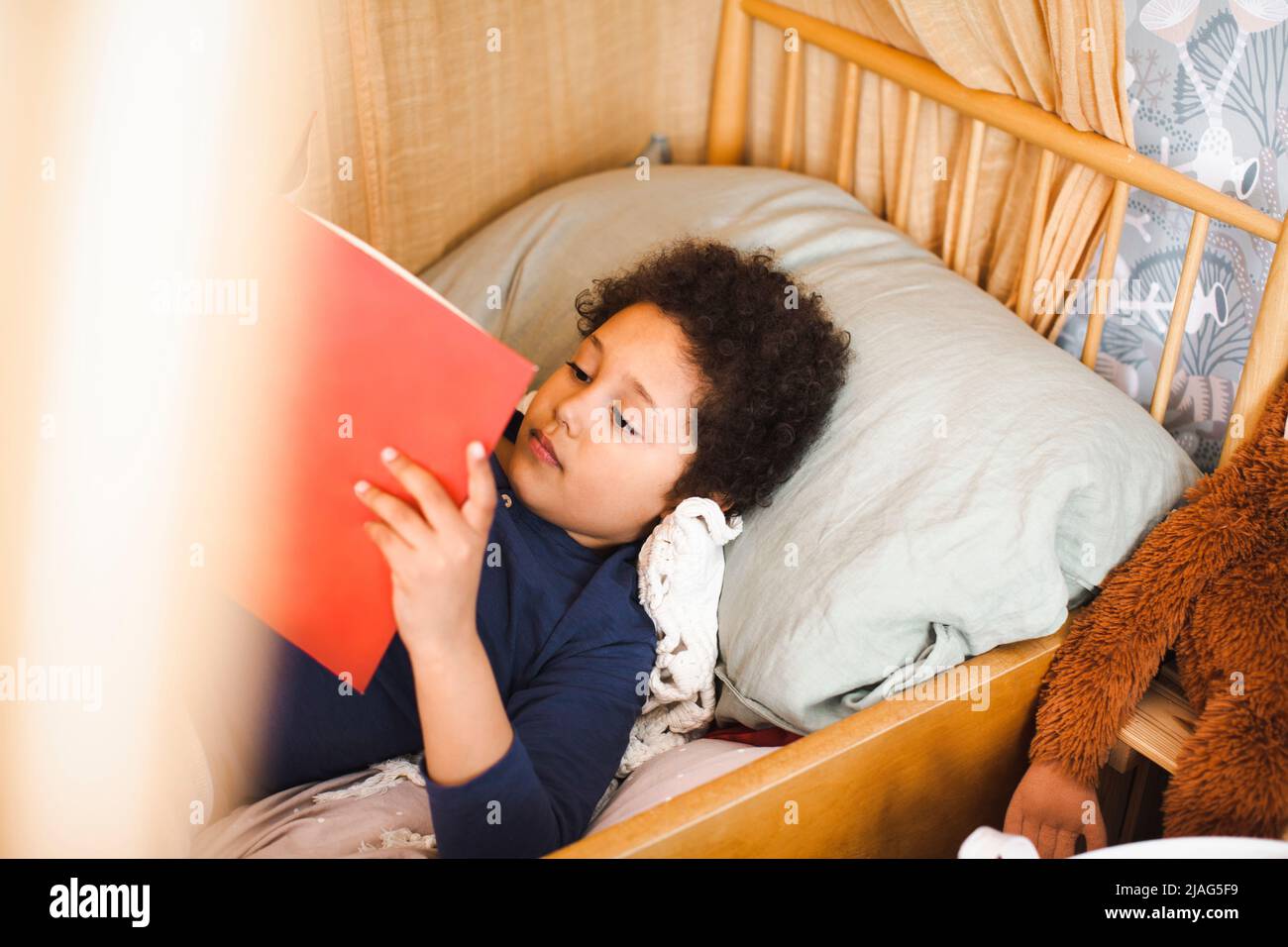 Vue en grand angle d'un garçon lisant un livre d'histoire en étant allongé sur le lit à la maison Banque D'Images