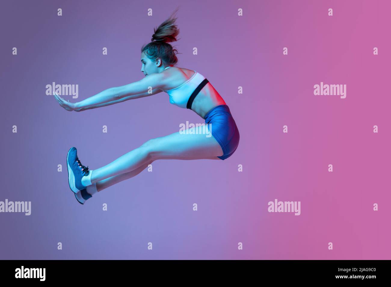 Moments. Jeune fille, athlète de formation technique de saut long isolé sur fond rose studio avec filtre bleu néon, lumière. Concept d'action Banque D'Images