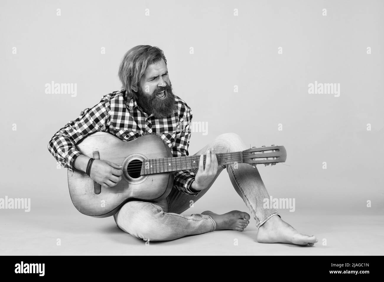 un musicien solitaire. joyeux et beau homme mature jouant de la guitare et souriant assis sur fond jaune. Portrait d'un homme à barbe heureux jouant Banque D'Images