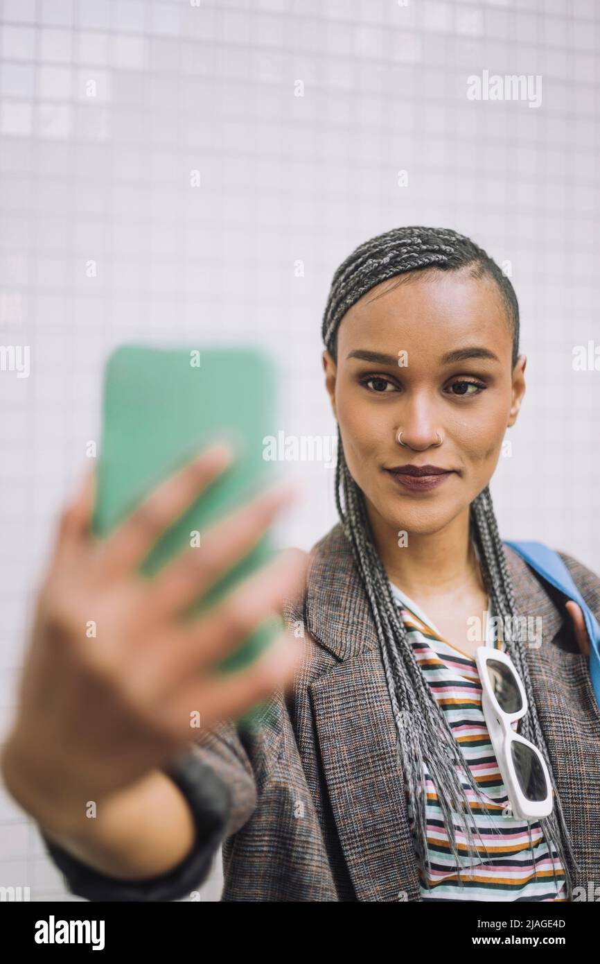 Femme souriante aux cheveux tressés prenant le selfie à travers le smartphone Banque D'Images