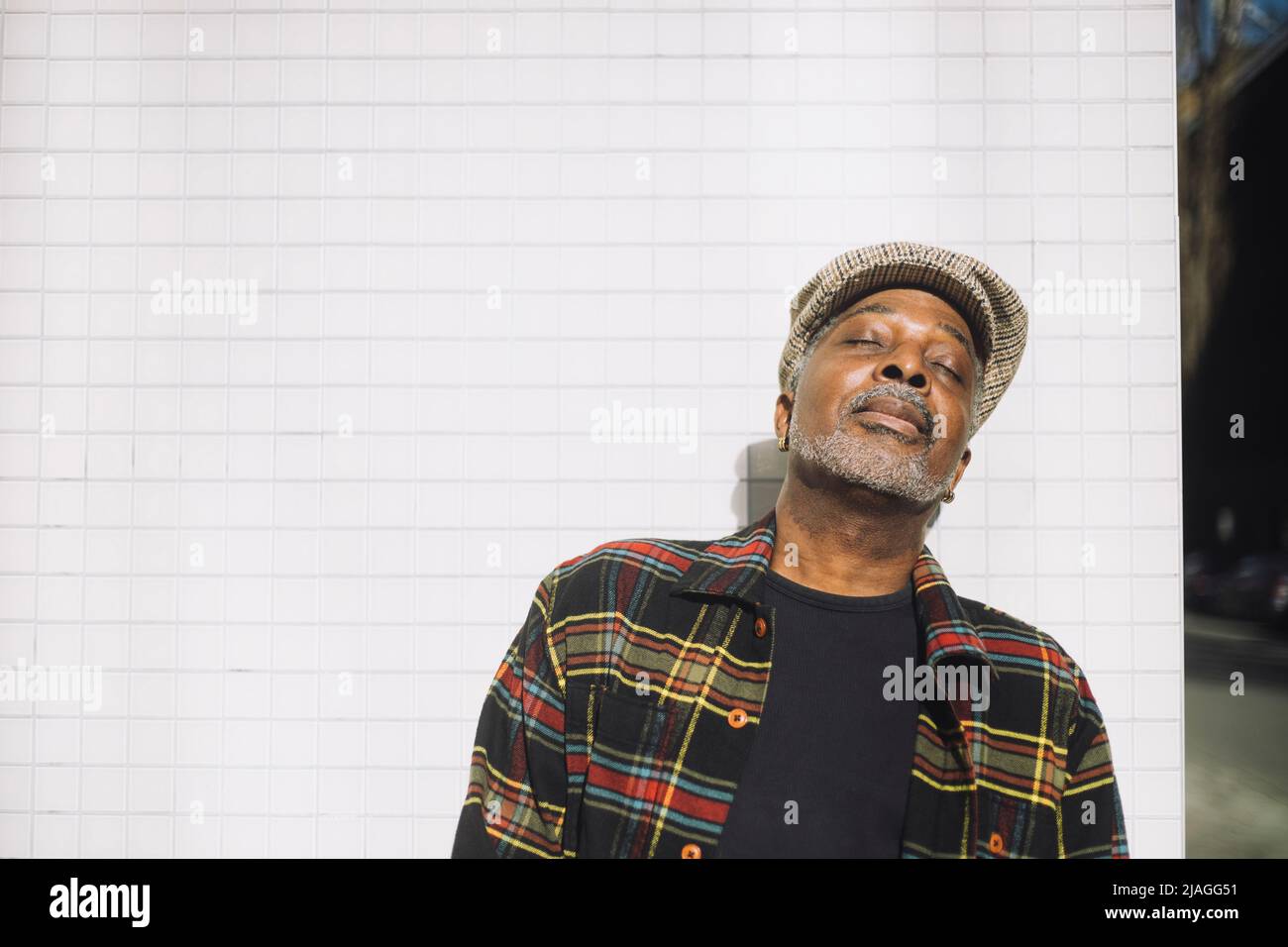 Homme mûr portant un capuchon plat en se tenant les yeux fermés contre le mur Banque D'Images