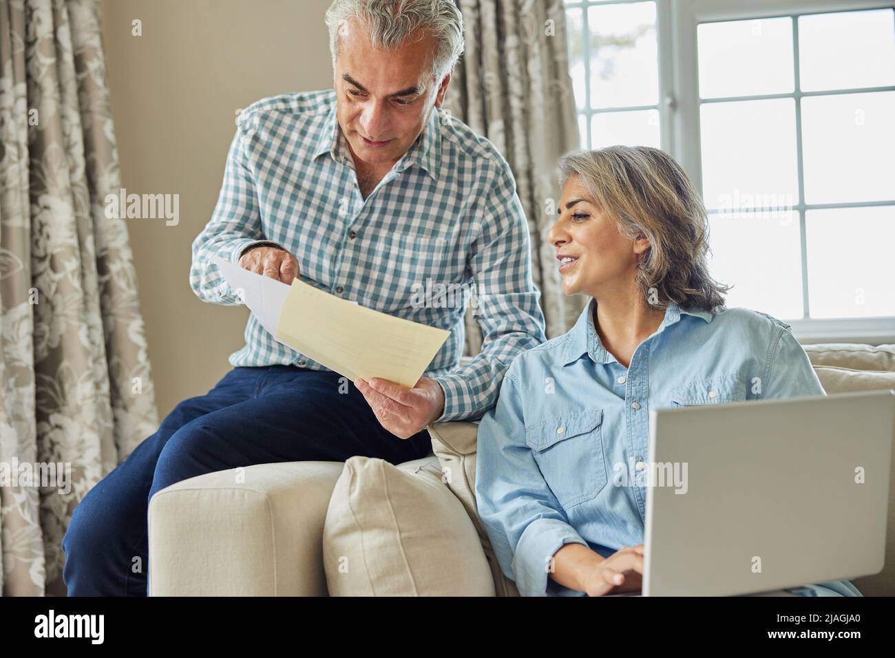 Souriant couple d'âge mûr à la maison examen des finances domestiques sur ordinateur portable Banque D'Images