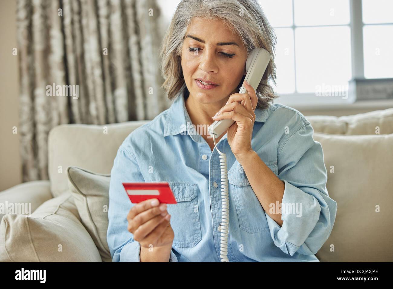 Femme mature à la maison donnant des détails de carte de crédit au téléphone Banque D'Images