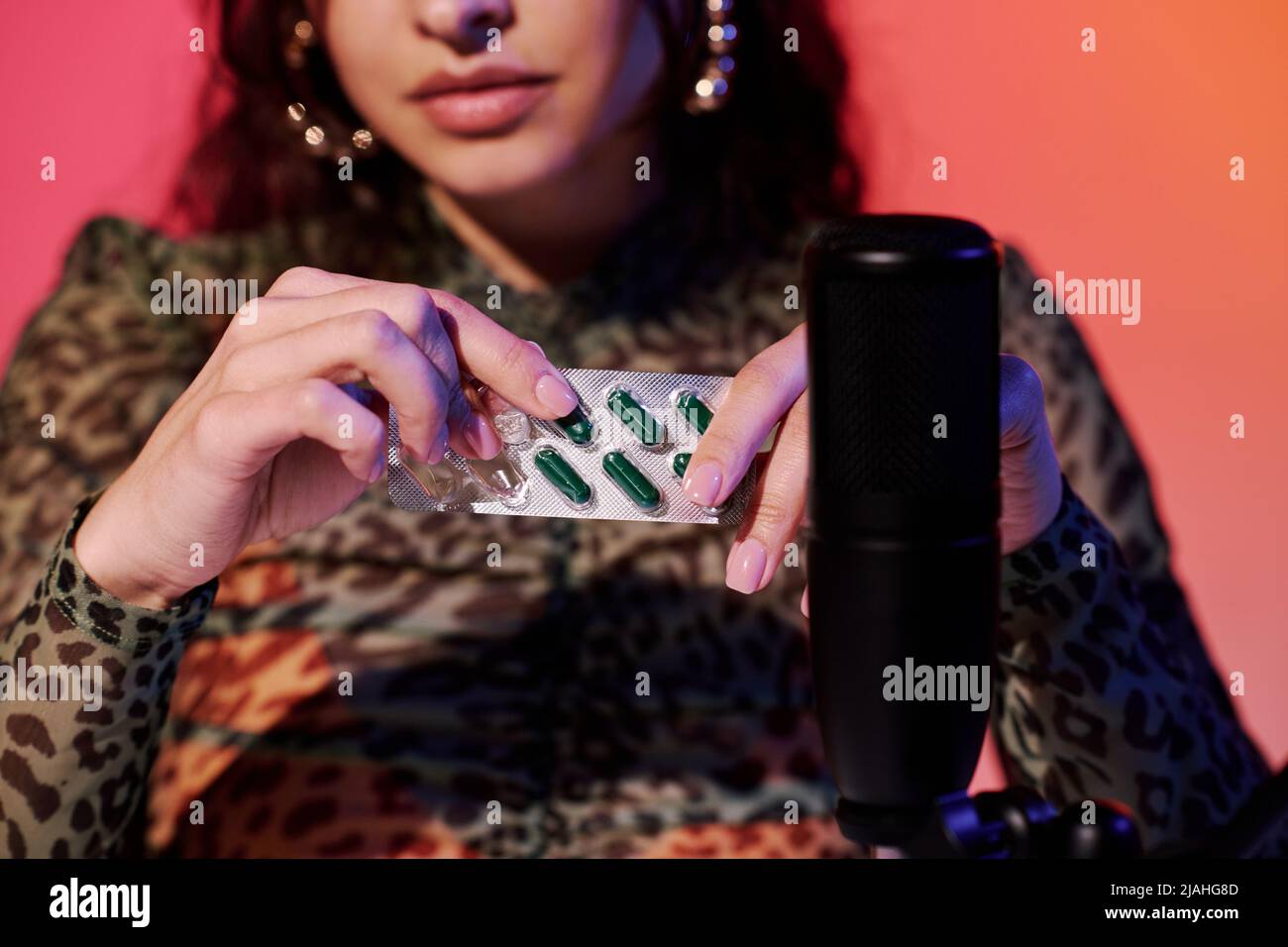 Jeune femme moderne assise en studio dans des sons d'enregistrement de lumière néon rose et jaune pour ASMR vlog en utilisant un blister pharmaceutique Banque D'Images