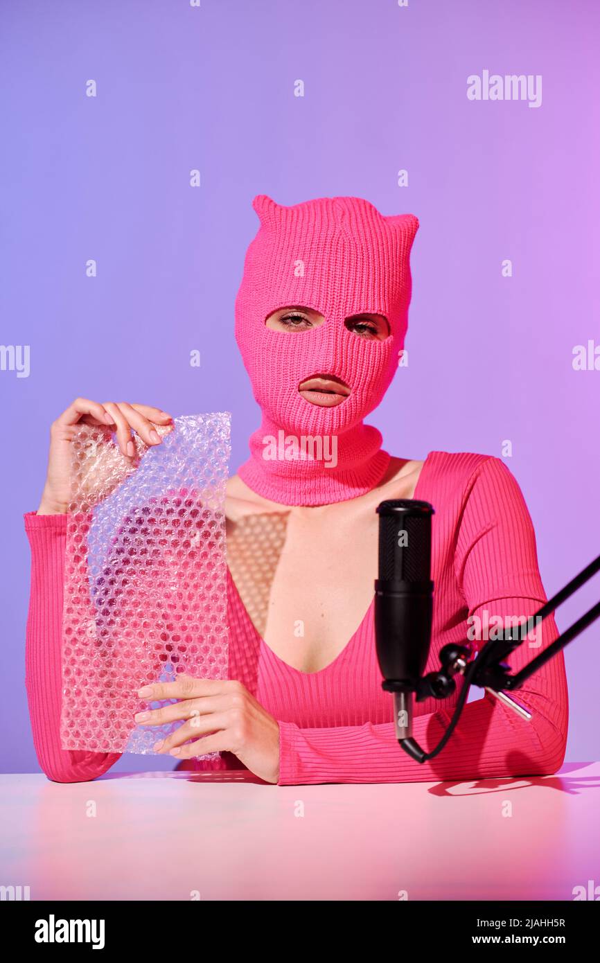 Jeune influenceur méconnaissable portant un chandail rose et un film à bulles de maintien en balaclava préparé pour le contenu ASMR Banque D'Images