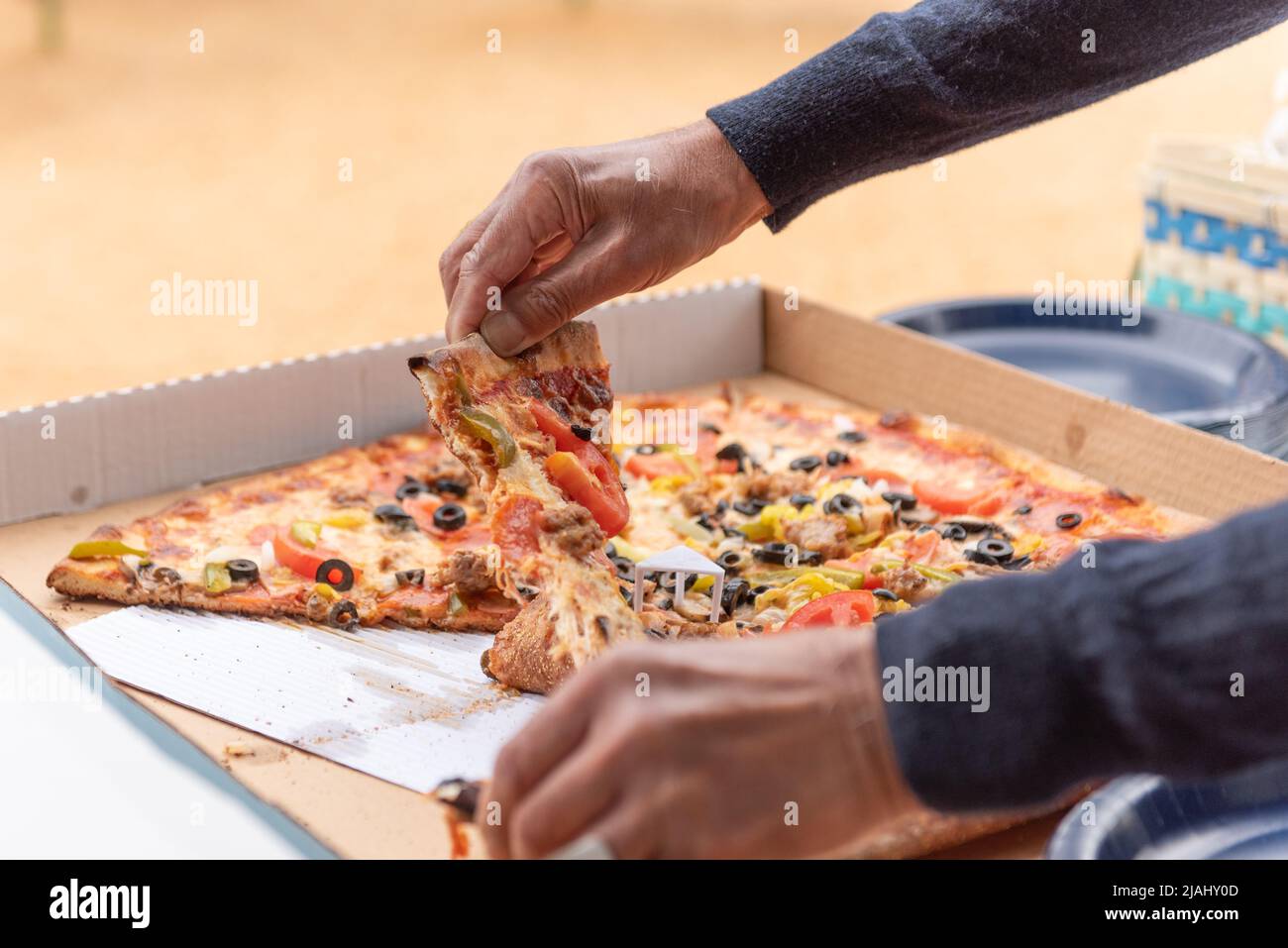 Mains d'un gardien de fête affamé tire une tranche de pizza hors de la boîte pour manger. Banque D'Images