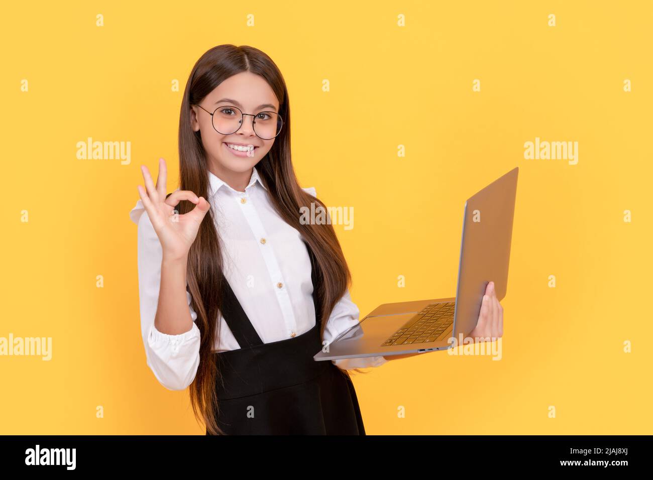 enfant heureux dans l'uniforme d'école et des lunettes étude sur ordinateur portable avec geste ok, e-learning Banque D'Images