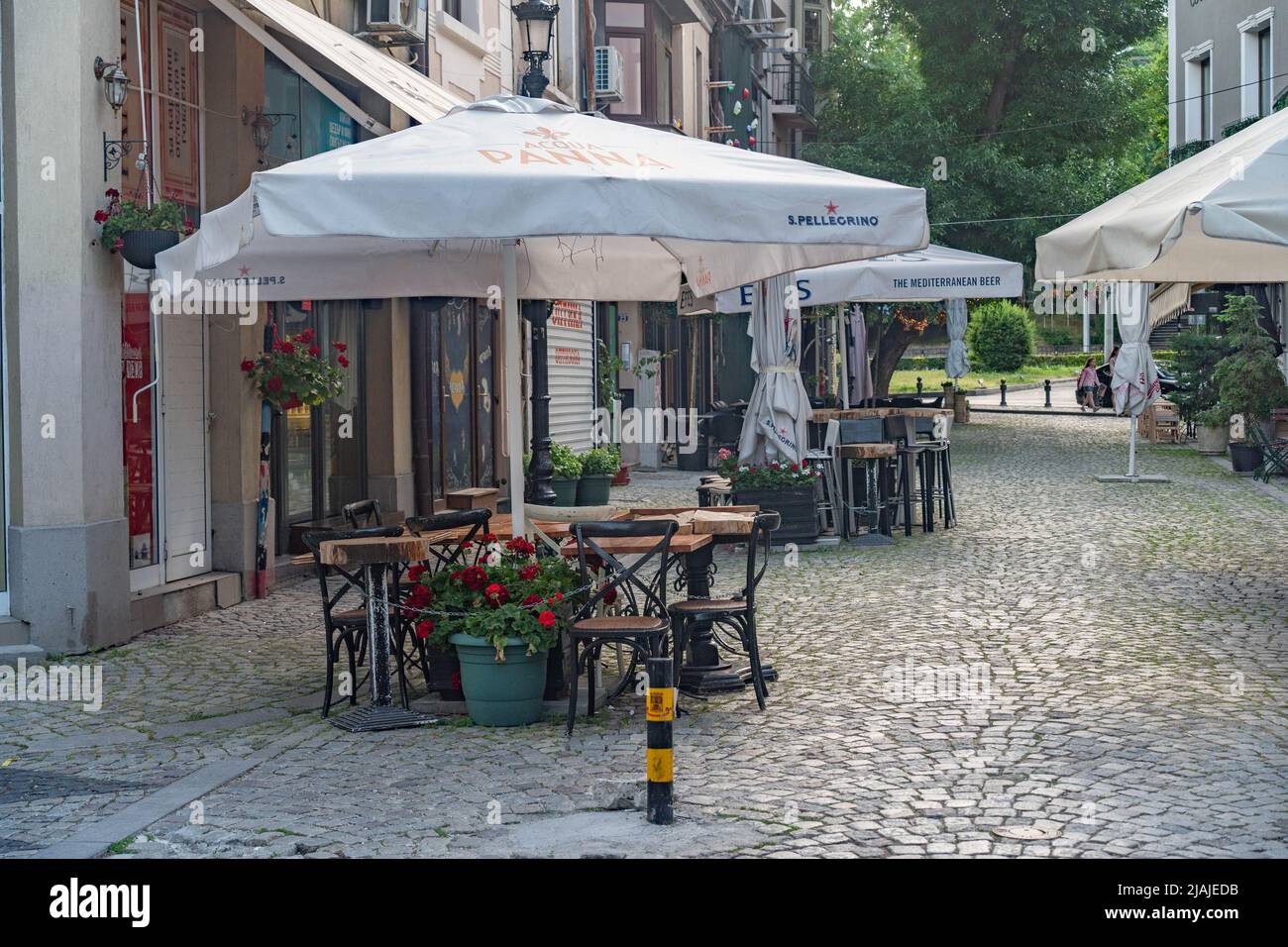 Plovdiv, Bulgarie - 22.05.2022: Café de rue pavée avec des tables et des chaises vides rassemblés et parasols ouverts le matin à Plovdiv, Bulgari Banque D'Images