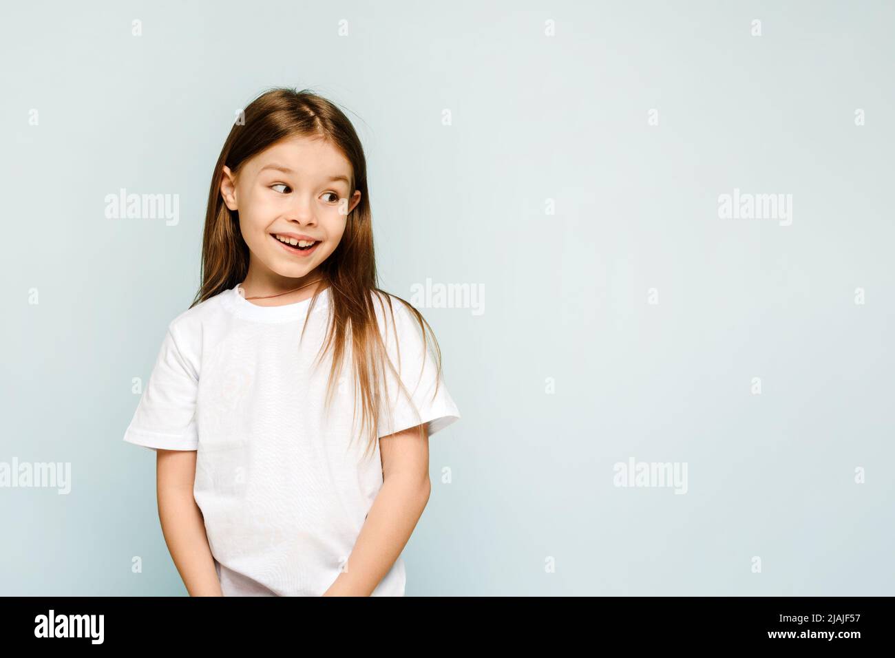 Une petite fille sur un fond bleu regarde loin avec surprise et joie. Espace de copie, place pour votre publicité. Banque D'Images