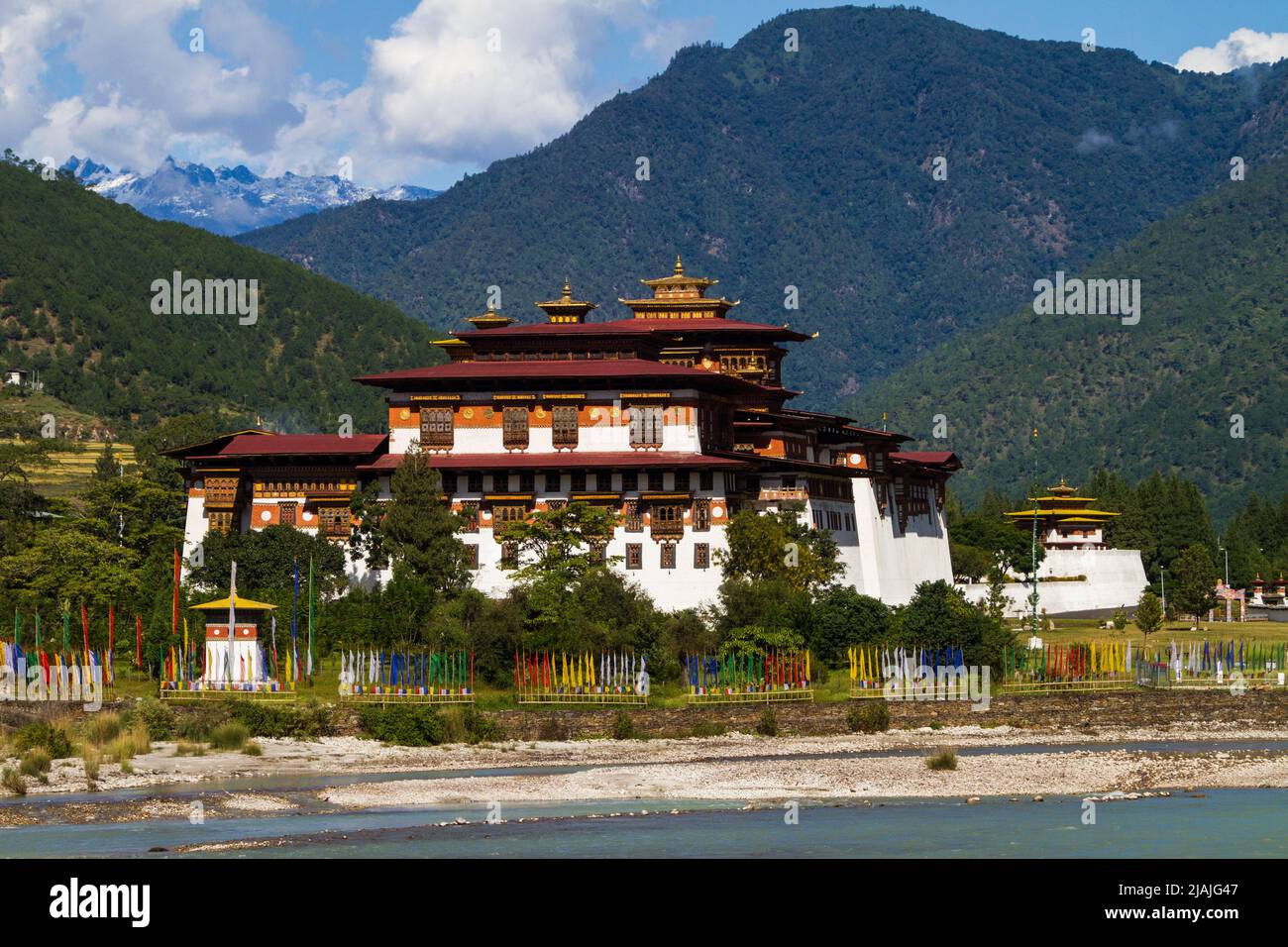 Le Punakha Dzong est vu à travers le Mo Chhu River dans le centre bouddhiste du Bhoutan tandis que les drapeaux de prières flottent à proximité Banque D'Images