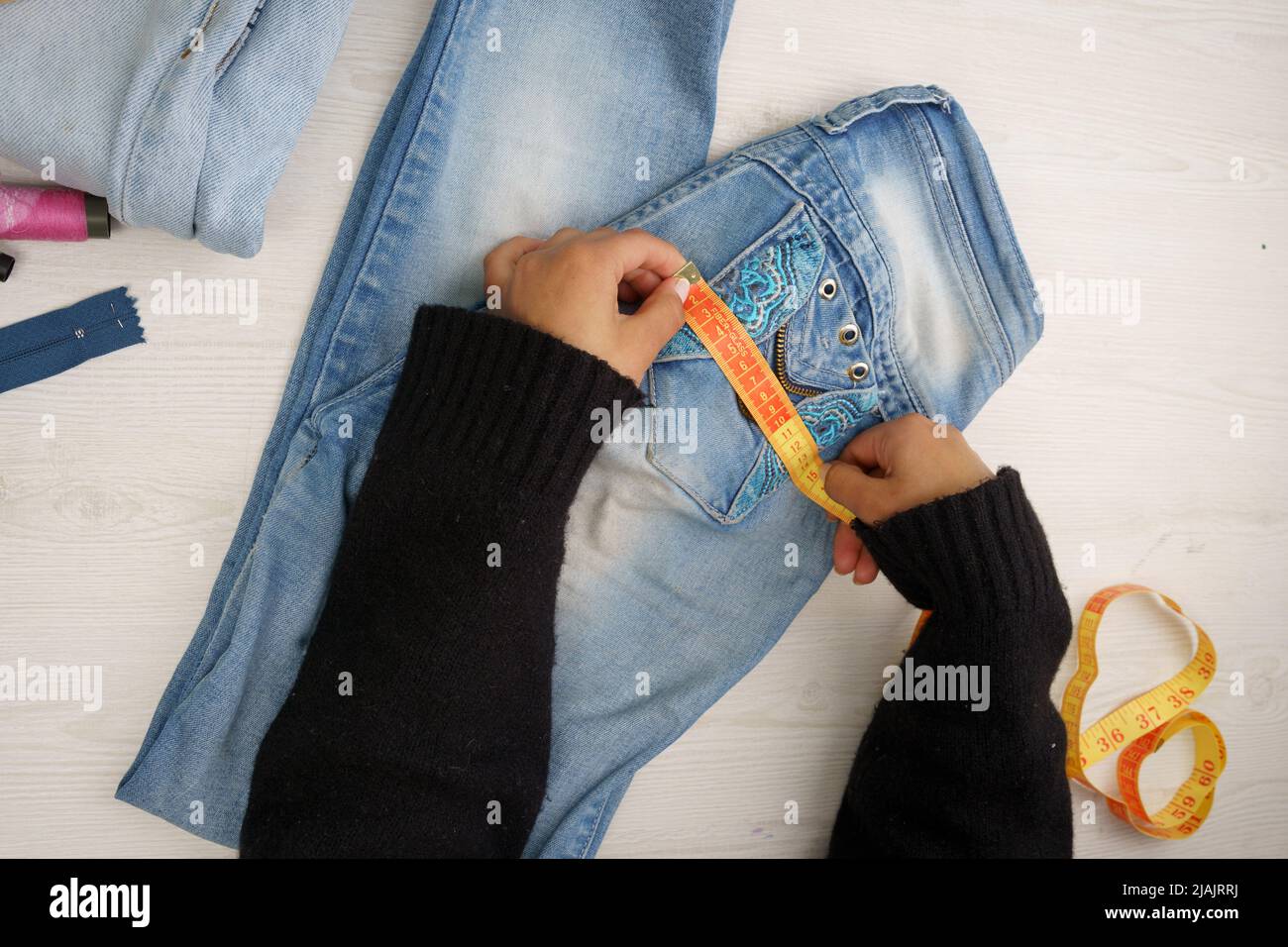 mains mesurant pour réparer un tissu de jean avec un mètre ruban, entouré  de fils de couleur, atelier de couture avec des instruments de travail  Photo Stock - Alamy