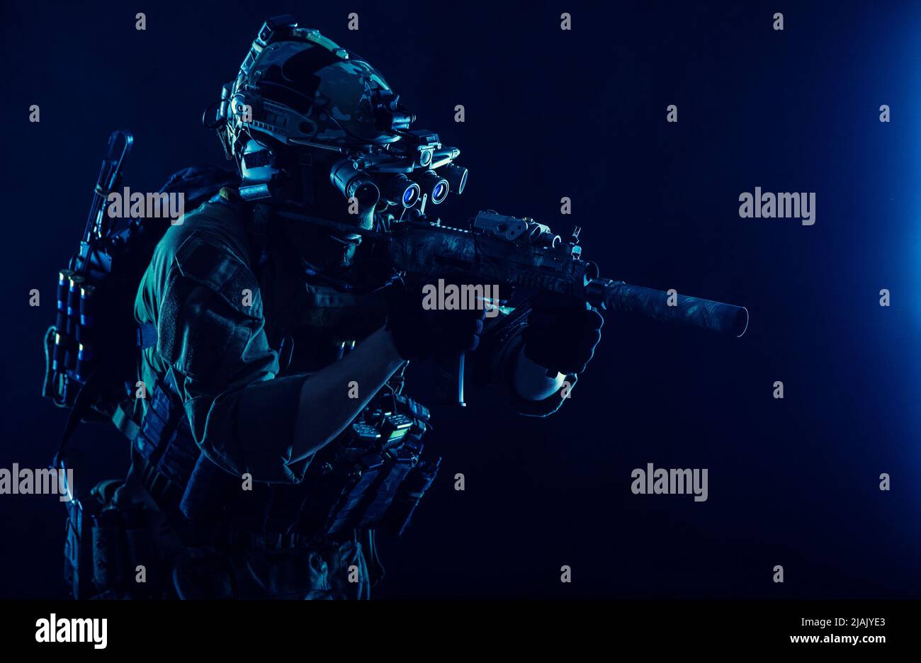 Un soldat des opérations spéciales portant un dispositif de vision nocturne, visant un fusil d'assaut à canon court dans l'obscurité. Banque D'Images