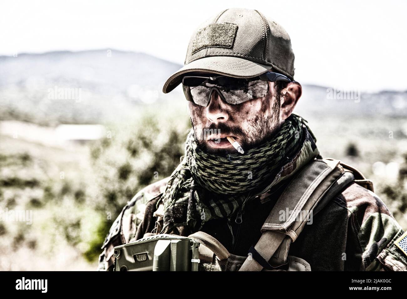 Soldat au visage sale fume une cigarette, portant des lunettes balistiques et une casquette de baseball. Banque D'Images