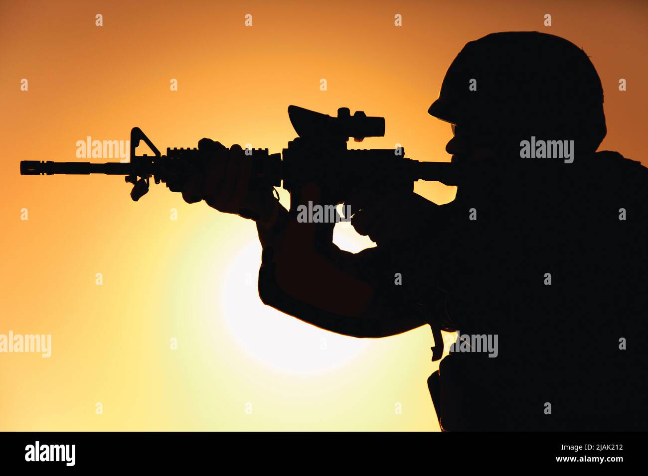 Silhouette d'un soldat tirant une carabine d'assaut contre un ciel nocturne ensoleillé. Banque D'Images