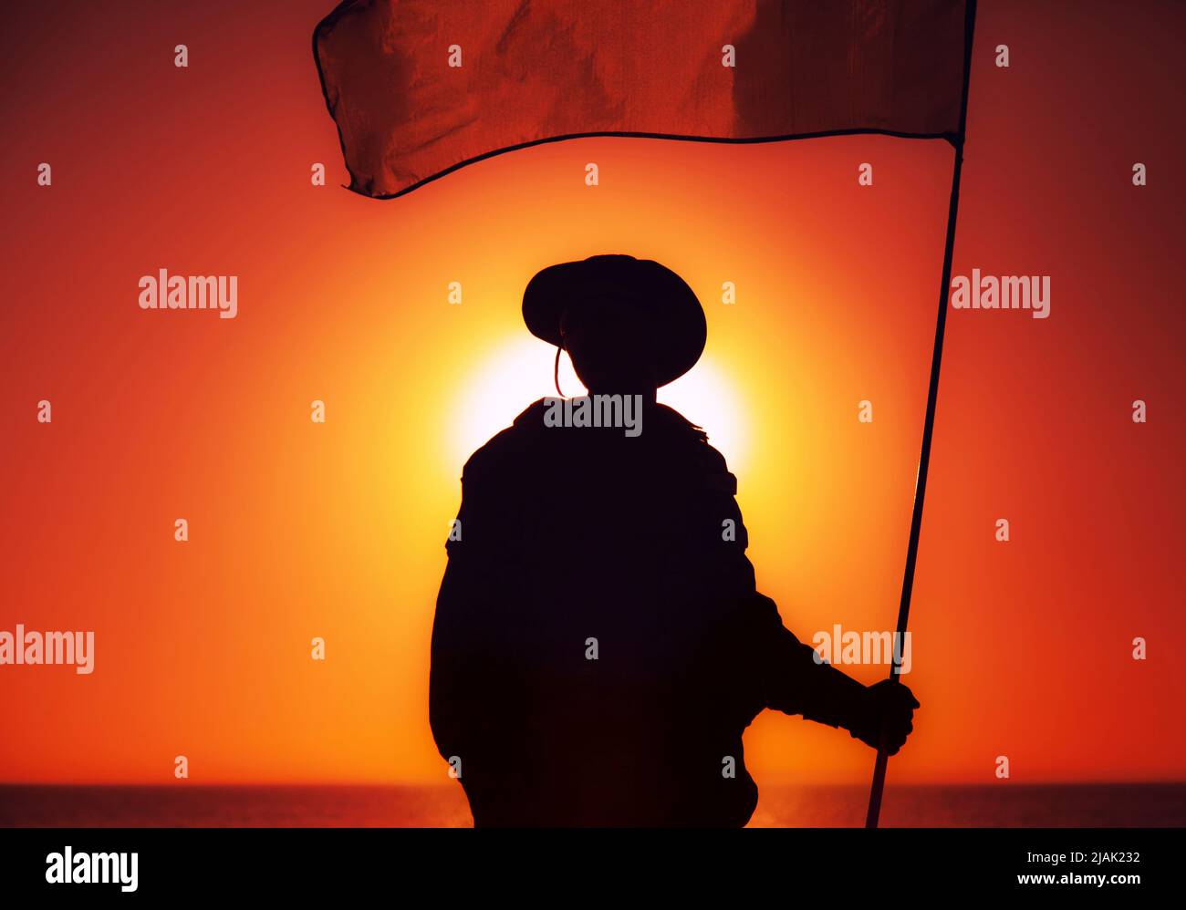 Silhouette d'un soldat qui agite le drapeau contre un ciel de coucher de soleil. Banque D'Images