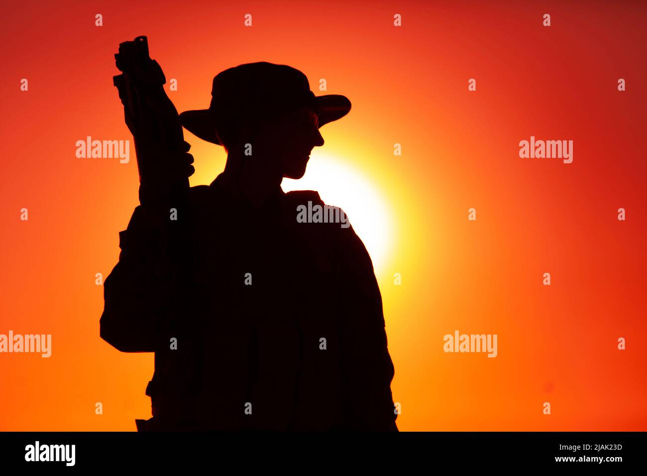 Silhouette d'un soldat debout avec un fusil de sous-machine bullpup contre un ciel de coucher de soleil. Banque D'Images